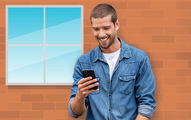 Man smiling at his phone in front of brick building with window